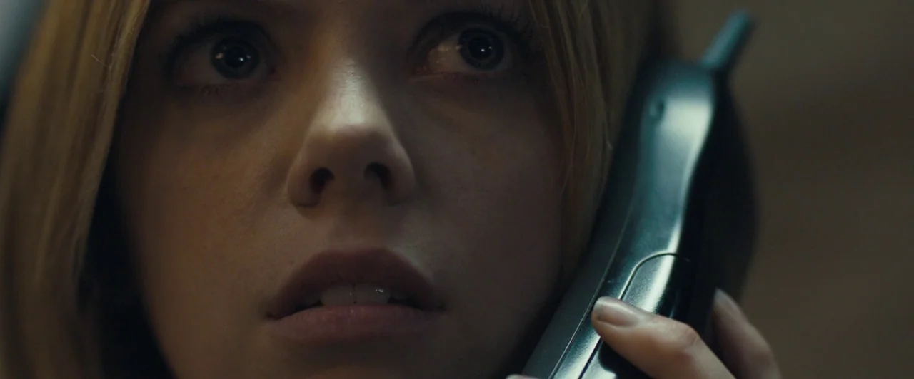 Compliance (2012) movie still: closeup — A close-up view of a woman holding a phone against her face. She looks upward with wide eyes while holding…