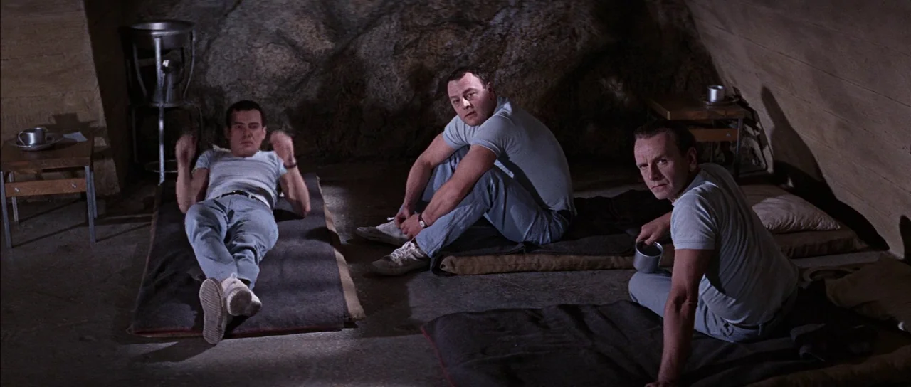 You Only Live Twice (1967) movie still: wide — A stone-walled room features thin sleeping mats arranged on a concrete floor surface. Three men…