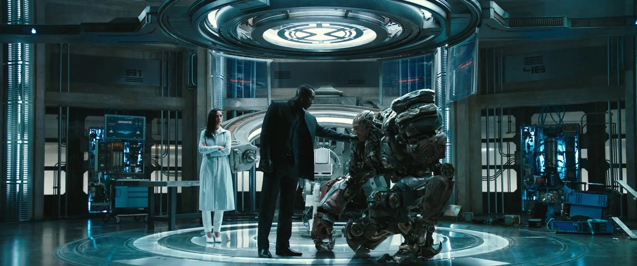 Alita: Battle Angel movie still: wide — A high-tech laboratory with circular platforms and glowing digital displays integrated into the walls. A man…