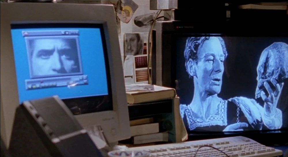 Hamlet (2000) movie still: medium — A cluttered desk features a 1990s computer monitor and a television screen side-by-side. The computer display…