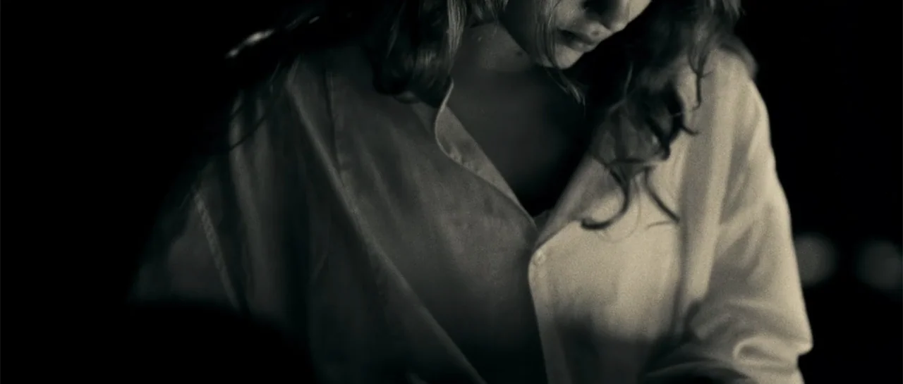 Blood Creek (2009) movie still: medium — A dimly lit room provides a dark background for the subject. A woman wearing a white shirt faces downward…