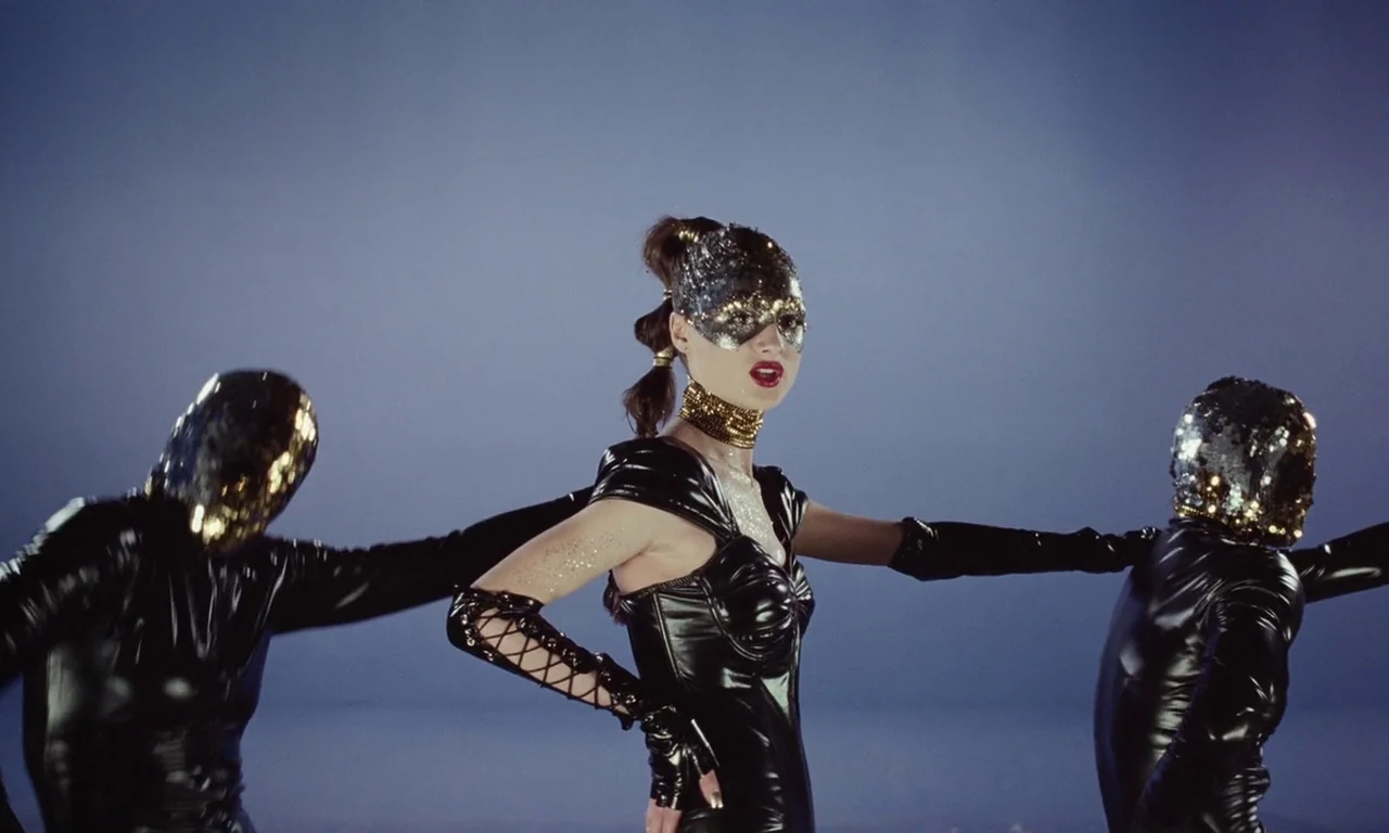 Vox Lux (2018) movie still: medium — A minimalist studio space with a flat gray background and bright artificial lighting. A woman in a black corset…