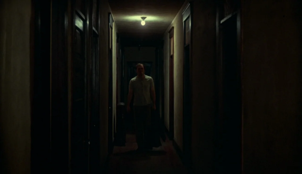 Fat City (1972) movie still: wide — A long, dark apartment building hallway features a series of closed wooden doors. A man walks forward toward the…