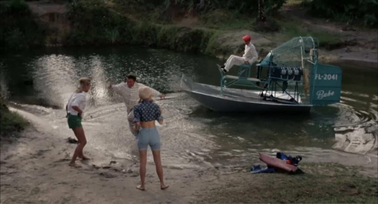 Cottonpickin' Chickenpickers (1967) movie still: wide — A natural swamp clearing features a narrow riverbank with dense vegetation and dark water.…