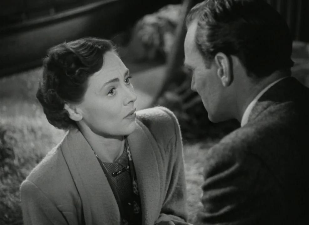Brief Encounter (1945) movie still: medium — A dimly lit indoor space featuring a man and a woman in conversation. The woman looks toward the man…