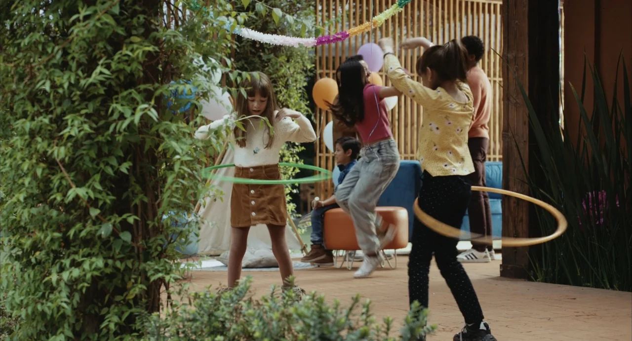 The Diary (1999) movie still: medium — A sunlit patio features wooden slats, party balloons, and a small play tent. Several children play with hula…