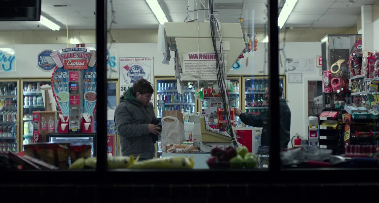 Manchester By The Sea (2016) movie still: medium — A cluttered convenience store checkout area with fluorescent lights and various product…