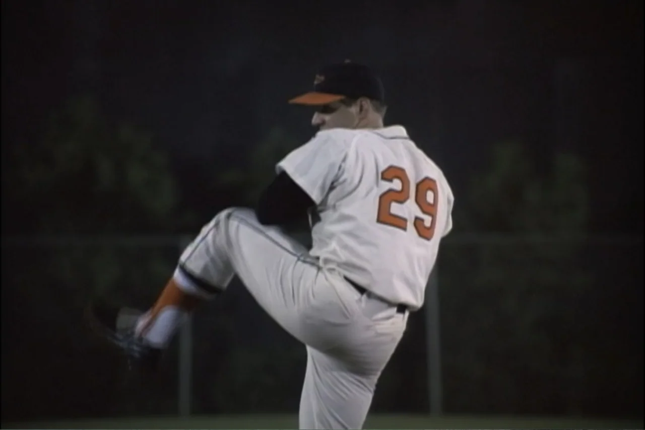 Unification of Japan 61 (2024) movie still: medium — A baseball player in a white uniform stands on an outdoor pitching mound at night. The pitcher…