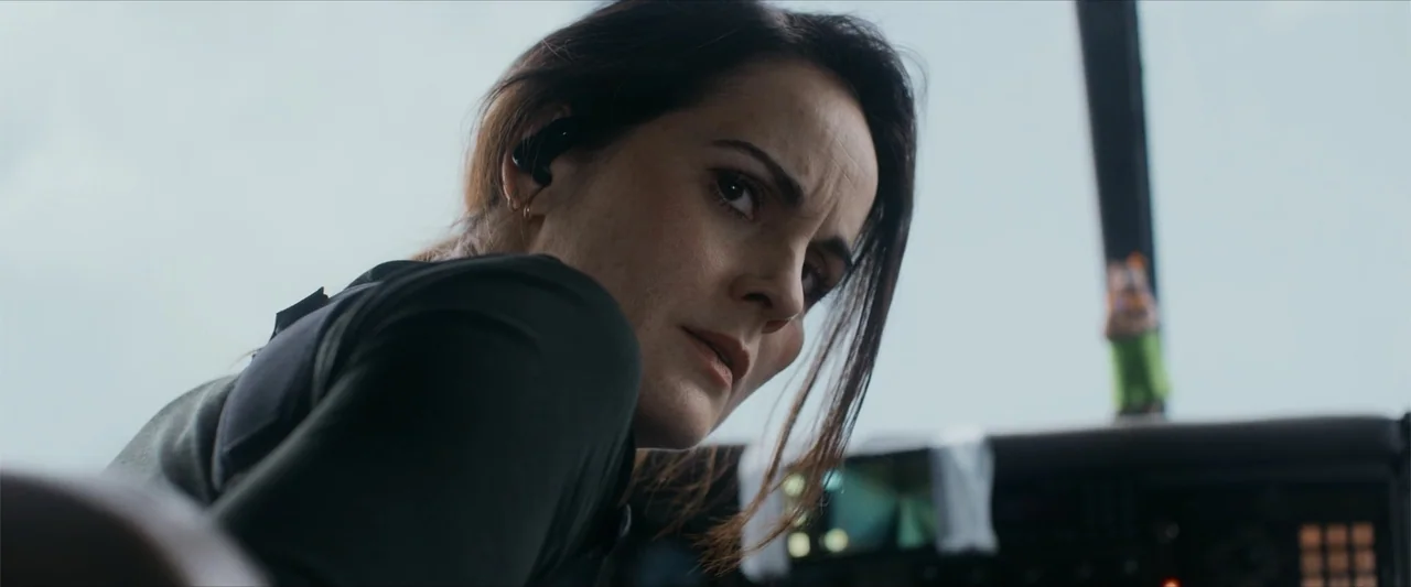 Flight Risk (2025) movie still: closeup — An aircraft cockpit interior with complex instrument panels and a window showing bright sky. A woman in…