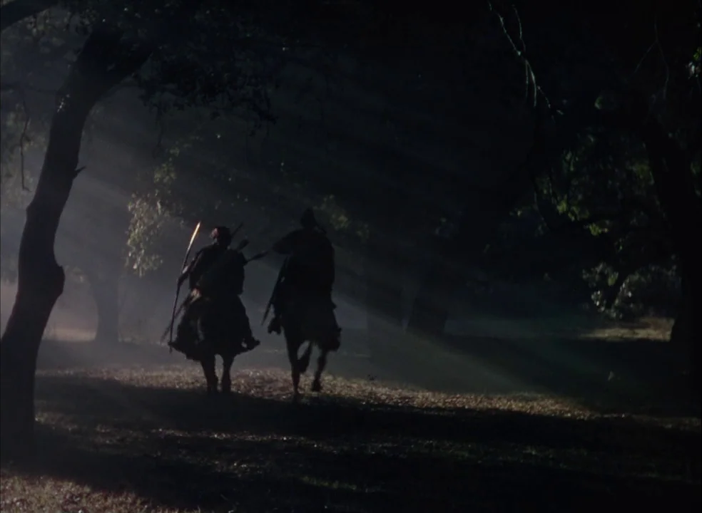 The Adventures of Robin Hood (1938) movie still: wide — Two riders on horseback traverse a dense, foggy woodland path during the day. Light filters…
