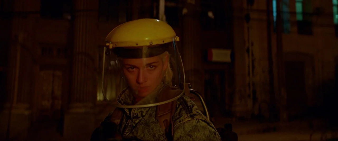 Ema (2019) movie still: medium — A dark city street at night is bathed in warm, artificial orange illumination. A person wearing a yellow safety…