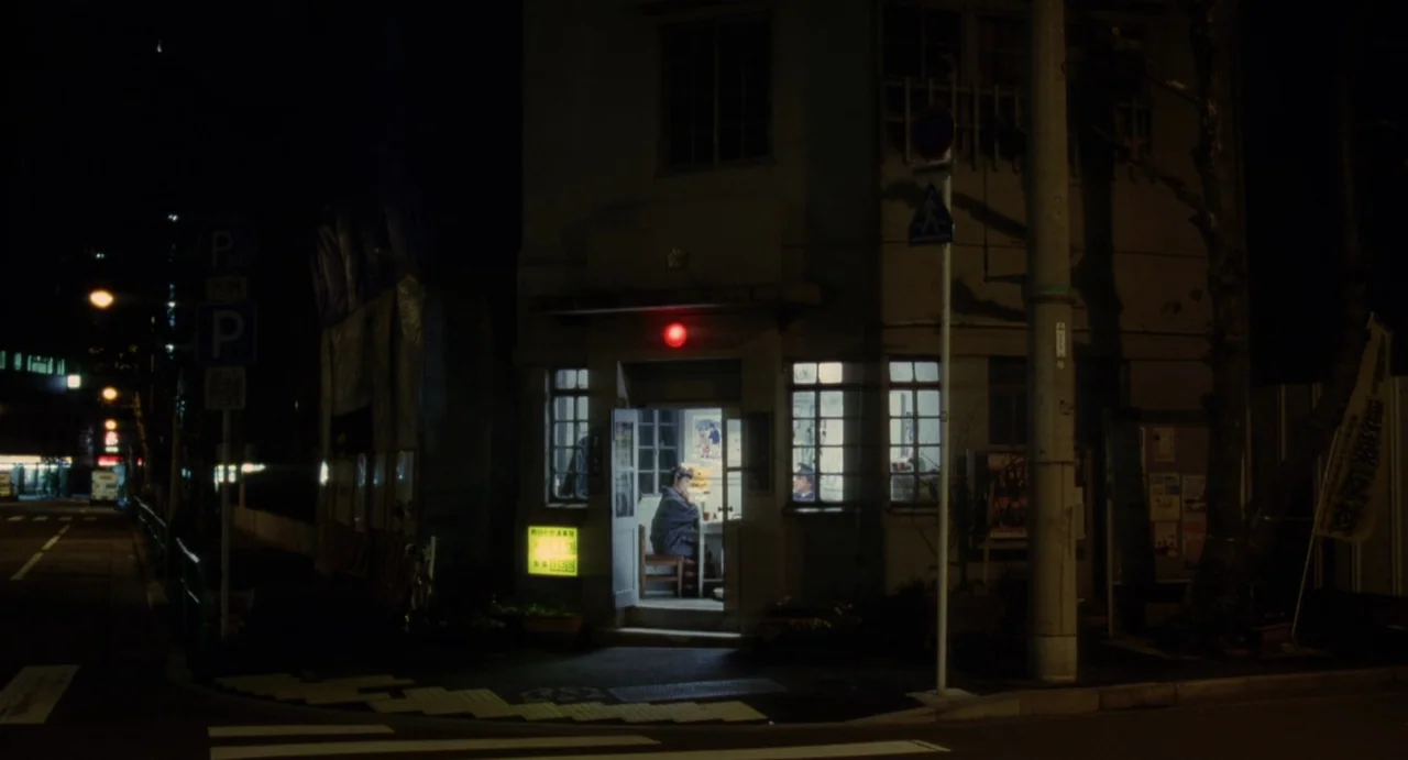 Air Doll (2009) movie still: wide — A dark street corner features a small lit police box at night. The interior is visible through an open door as a…