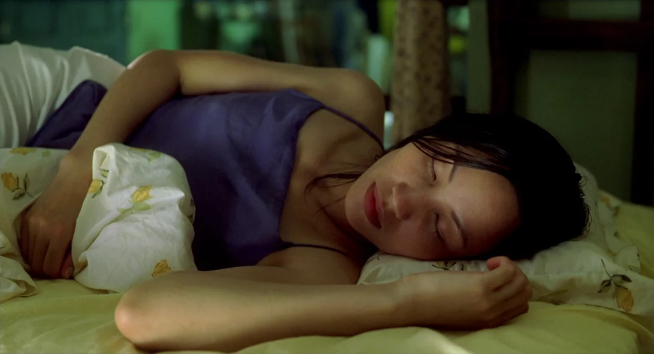 The Vertical Ray of the Sun (2000) movie still: closeup — A woman lies asleep in a bed with yellow floral patterned bedding. She is resting her head…