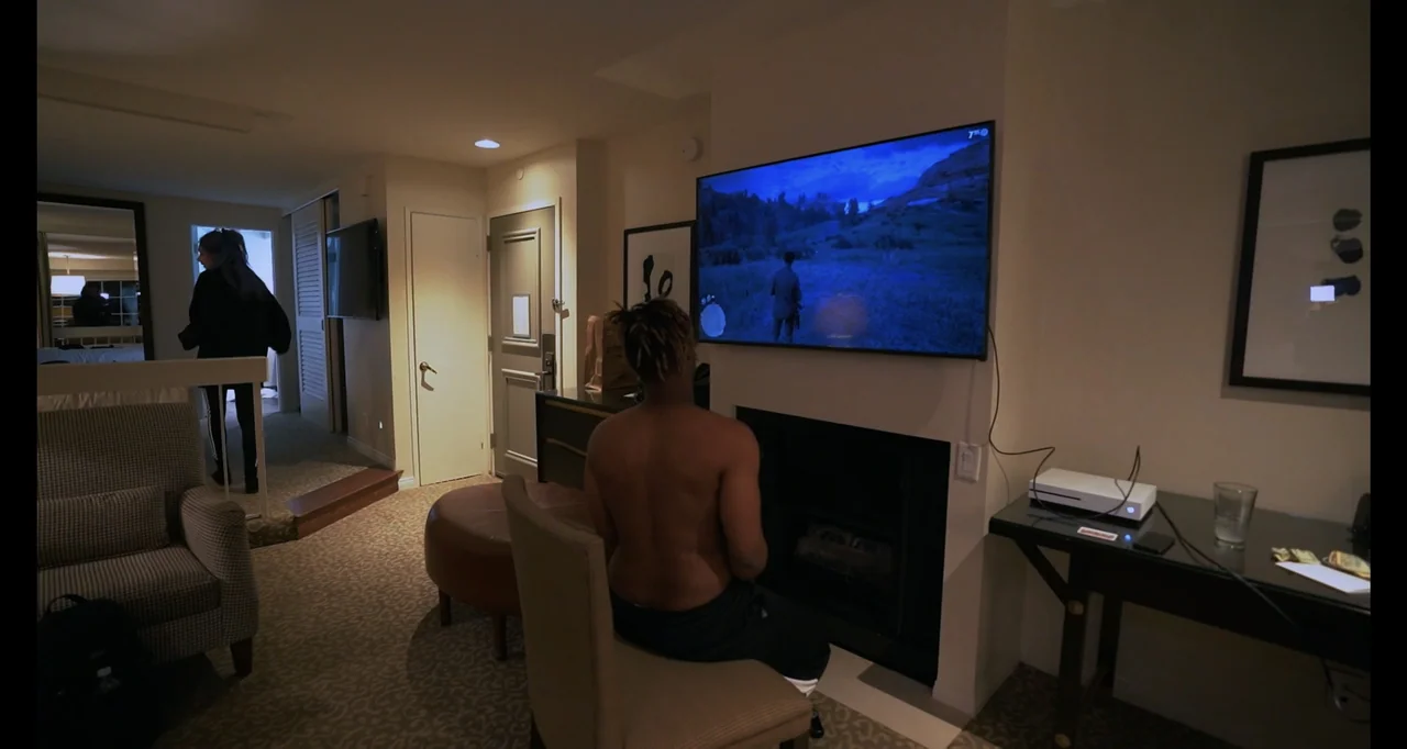 Juice WRLD: Into the Abyss (2021) movie still: medium — A modern hotel room features beige walls, patterned carpet, and a wall-mounted television…