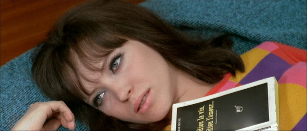 Made in U.S.A. (1966) movie still: closeup — A woman lies on a blue textured surface with a colorful checkered garment. She rests her head while…
