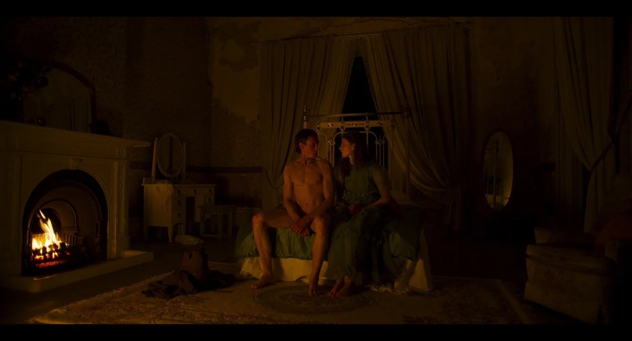 True History of the Kelly Gang (2019) movie still: fullbody — A dimly lit, dated room features a fireplace and a metal-framed bed. A man and woman…