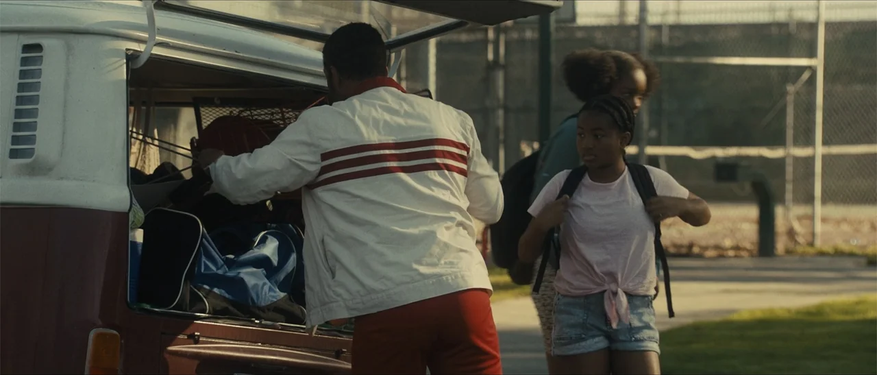 King Richard (2021) movie still: medium — An outdoor area with a chain-link fence visible in the background during golden hour. A man reaches into…