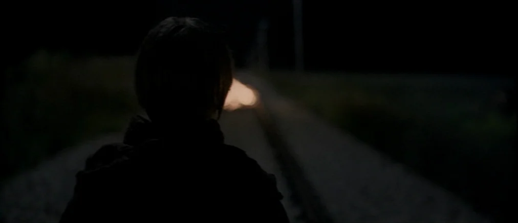 Time Of The Wolf (2003) movie still: medium — A dark, rural railway track stretches into the distance at night. A lone figure stands facing the…