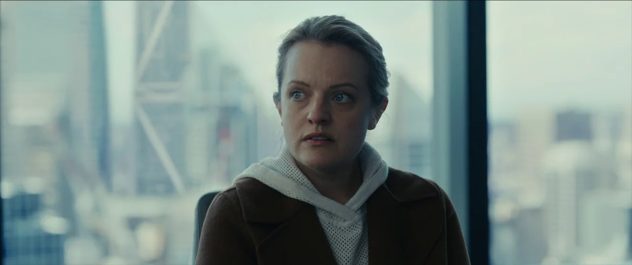 The Invisible Man (2020) (2020) movie still: medium — A woman stands in a modern, glass-walled skyscraper office with a blurred city skyline…