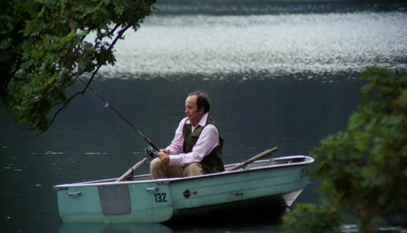 Let’s Scare Jessica To Death (1971) movie still: wide — An older man sits in a small, light blue rowboat numbered 132. He holds a fishing rod while…