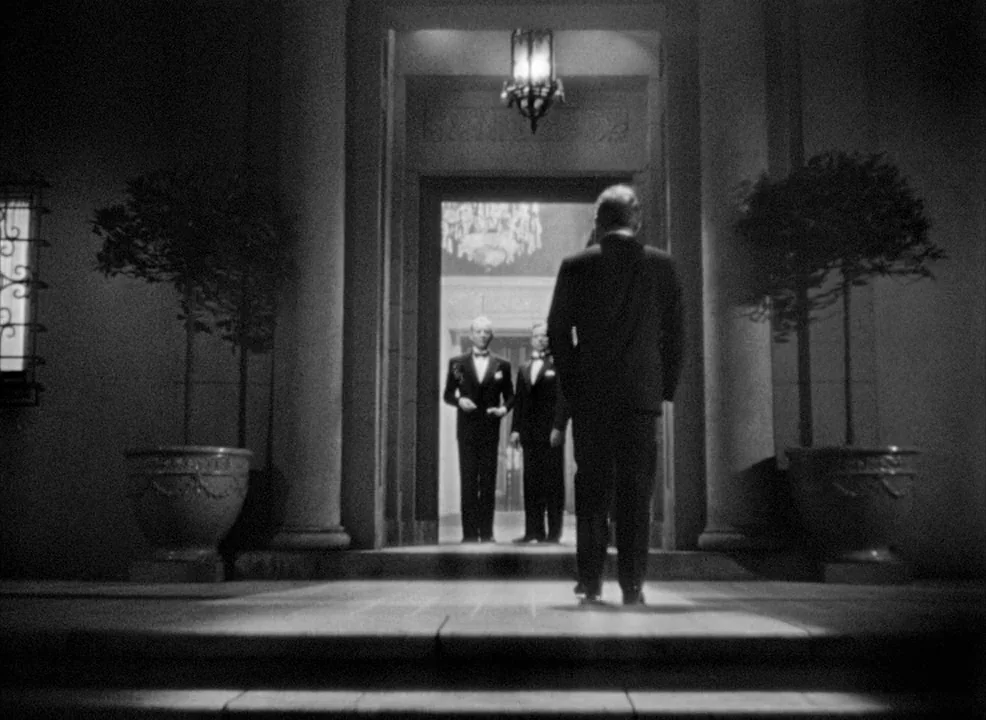 Notorious (1946) movie still: fullbody — A stone mansion entrance with large planters stands at the top of a staircase. Three men in formal evening…