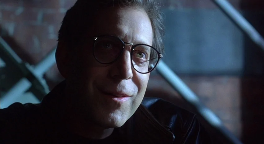 Double Happiness (1994) movie still: closeup — The background features dark brickwork and industrial steel beams in a dimly lit space. A man wearing…