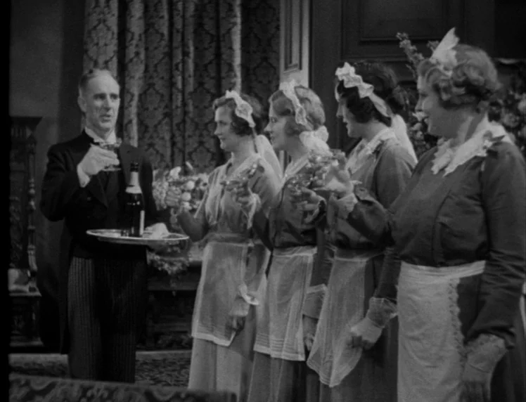 Frankenstein movie still: medium — A formal dining room features heavy curtains and decorative floral arrangements in the background. A butler…