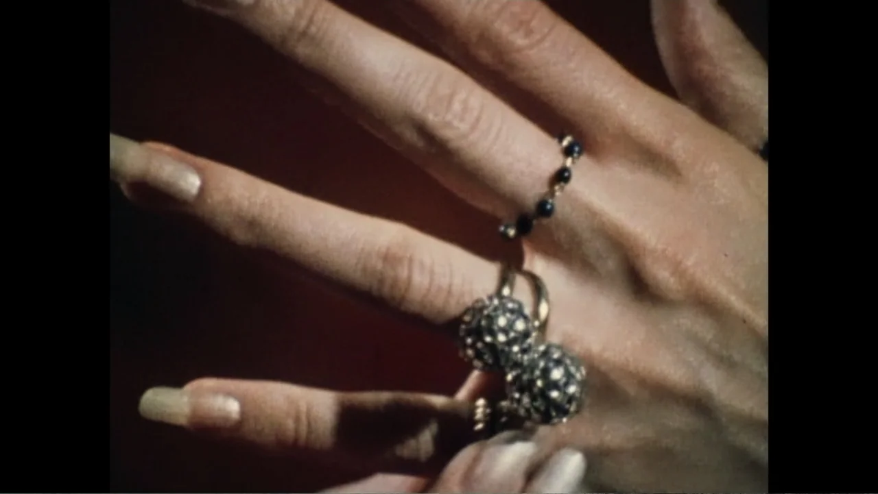 Dear Ms.: A Revolution in Print (2025) movie still: closeup — A close-up view of a hand wearing gold and gemstone jewelry against a red background.…