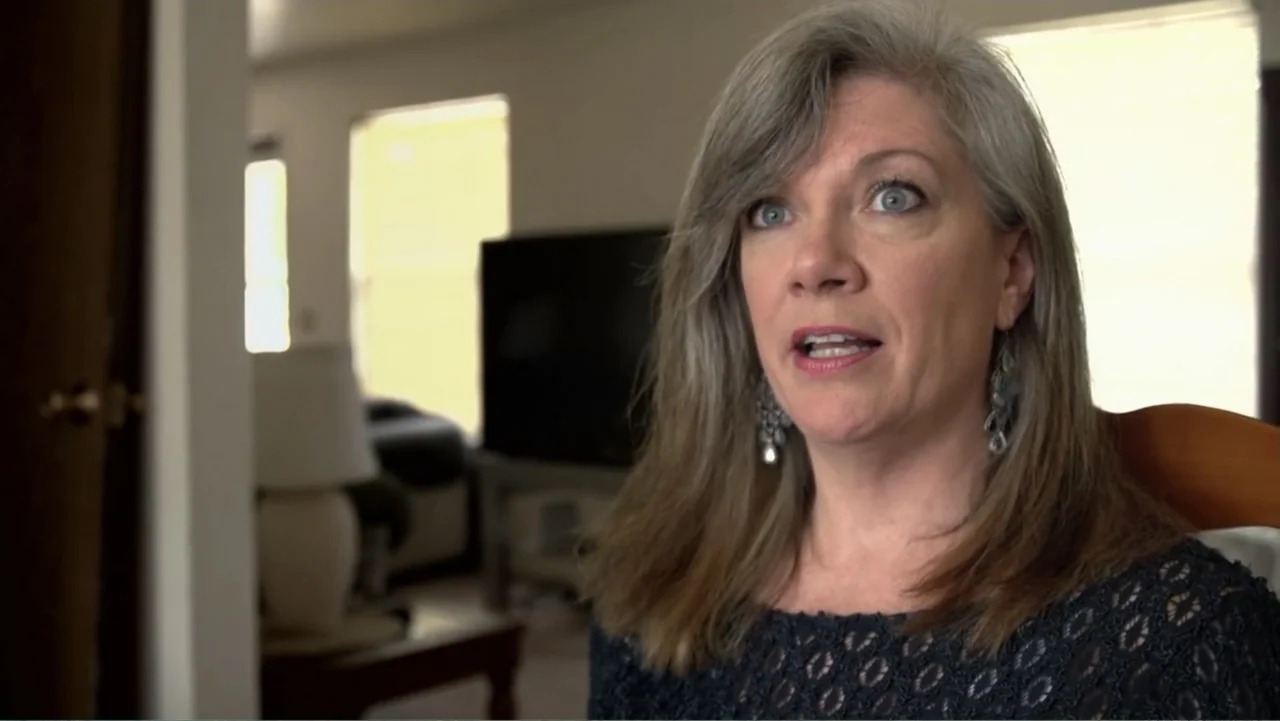 A Dangerous Son (2018) movie still: medium — A residential living room interior featuring blurred furniture and windows in the background. A woman…