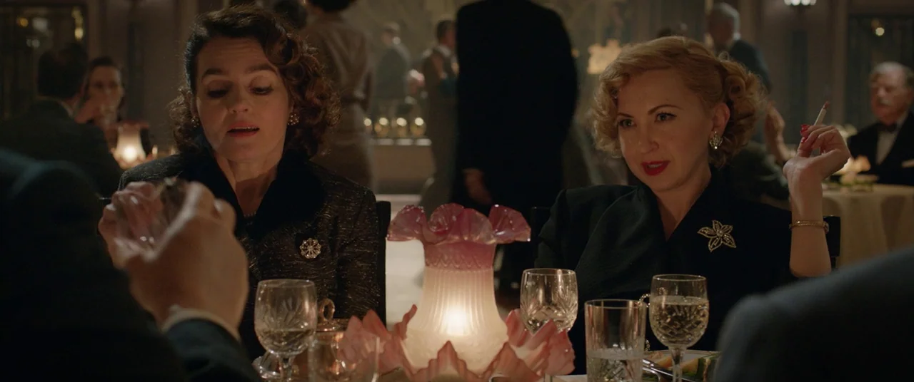 Domino (2005) movie still: medium — A dimly lit 1940s restaurant with multiple tables and patrons visible in the background. Two women in formal…