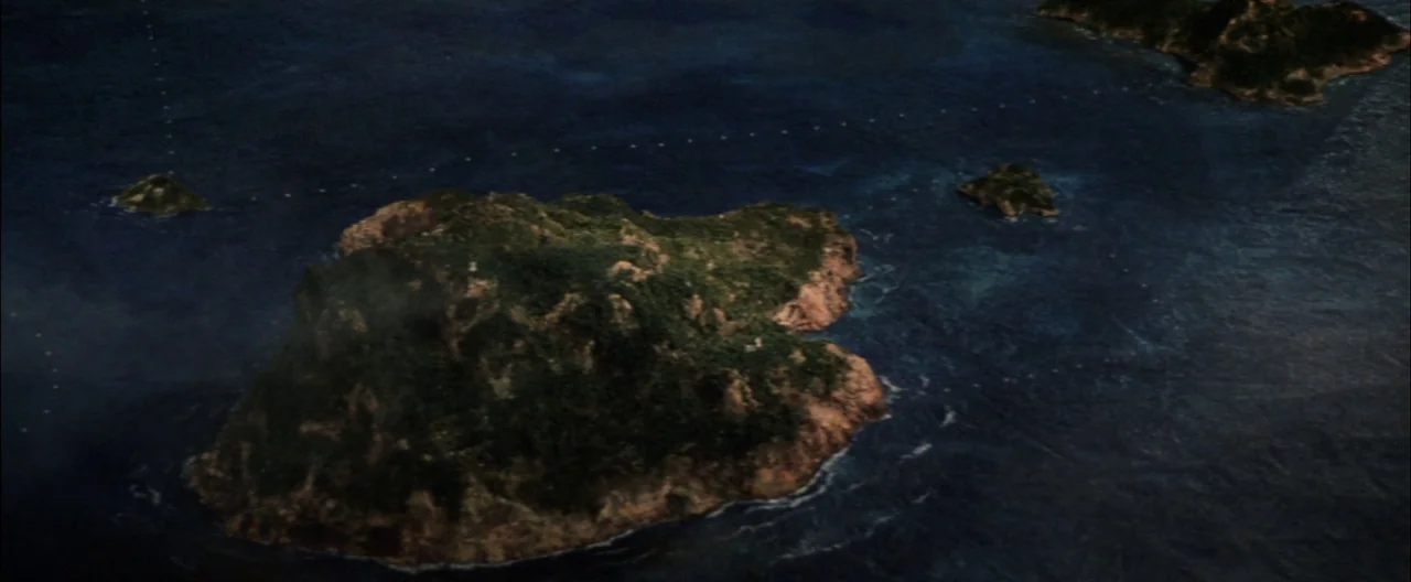 Destroy All Monsters (1968) movie still: establishing — An aerial view shows a collection of green islands surrounded by dark blue water. A faint…