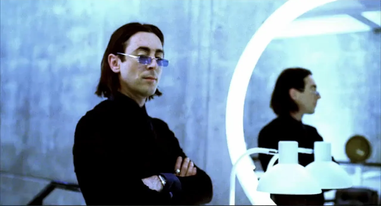 Josie and the Pussycats (2001) movie still: medium — An interior space with a concrete wall and a large circular lighted vanity mirror. A man in…