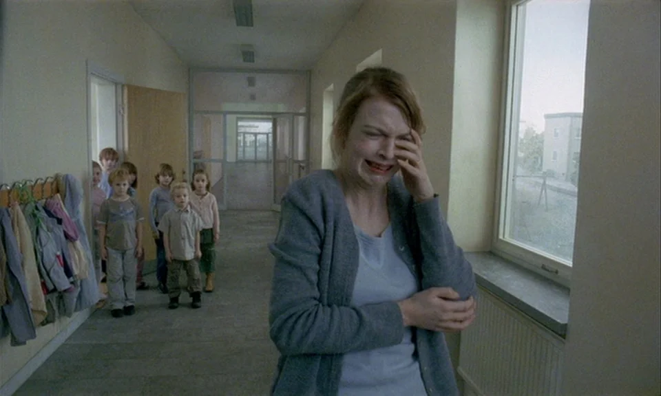 You, The Living (2007) movie still: medium — A quiet school hallway features pale walls with rows of children standing near doorways. A woman stands…