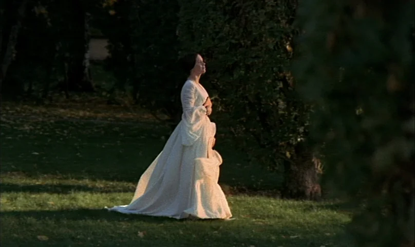 Cries and Whispers (1972) movie still: fullbody — A woman in a white historical dress walks across a grassy area. Trees are situated in the…