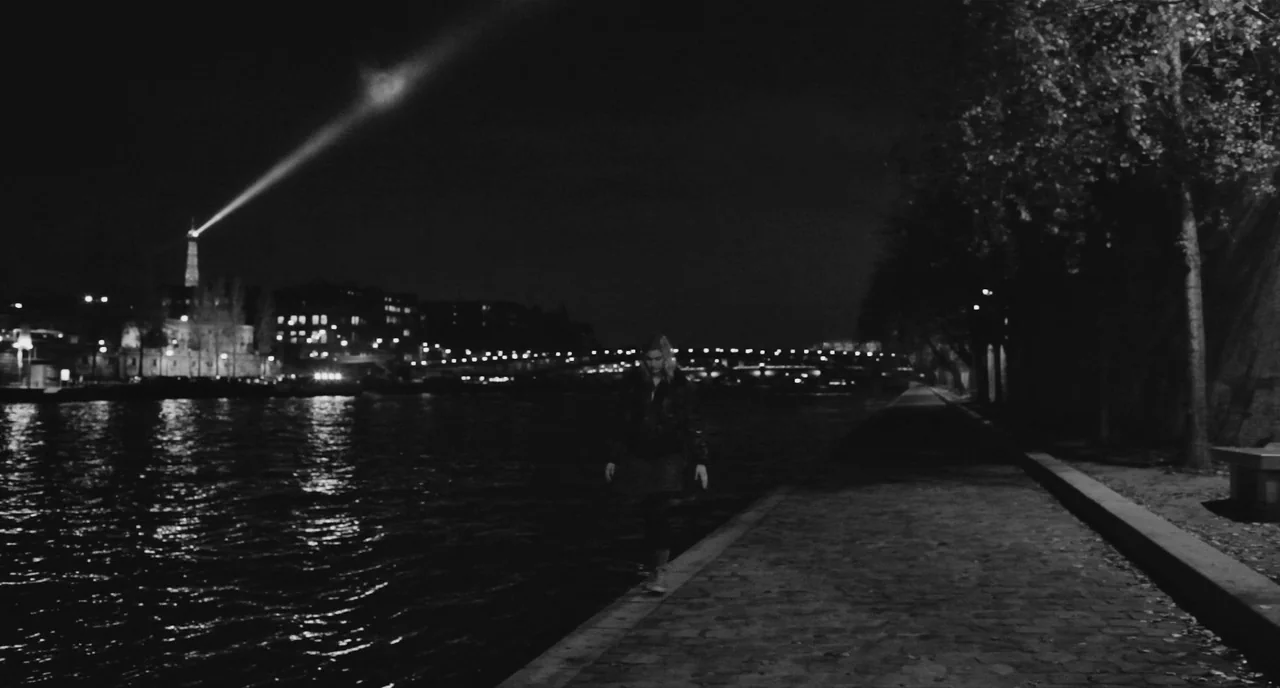 Frances Ha (2012) movie still: wide — A night view of a paved embankment running alongside the Seine river. A lone woman walks toward the camera…
