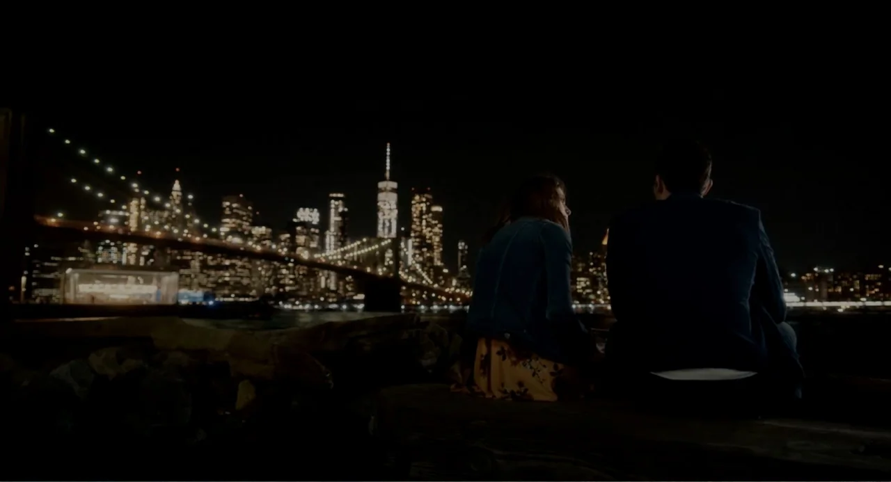 Can You Keep a Secret? (2019) movie still: fullbody — A dark wooden pier at night sits in the foreground with a blurred skyline visible. A man and a…
