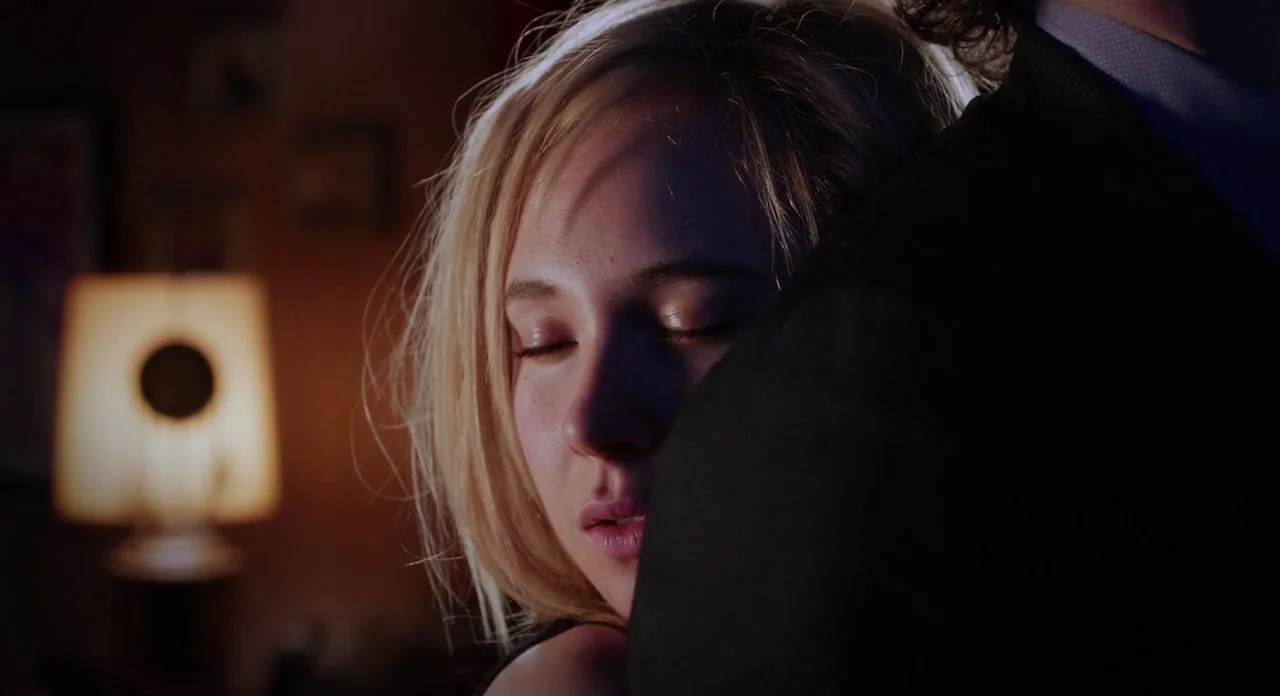 Killer Joe (2011) movie still: closeup — A dimly lit domestic interior features a glowing table lamp in the background. A woman with blonde hair…