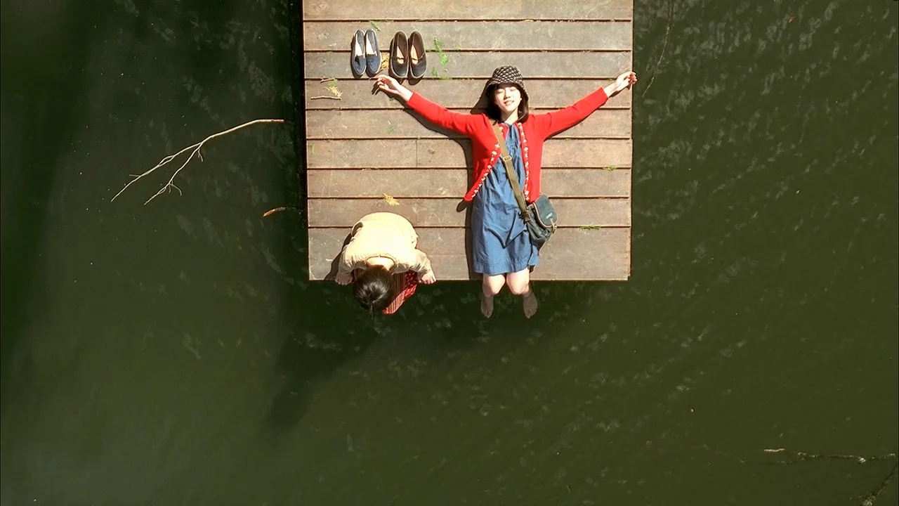 A Tale of Two Sisters (2003) movie still: wide — A wooden pier floats on the dark green surface of a still lake. A woman lies flat with her arms…