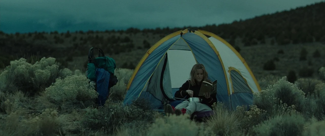 Wild (2014) movie still: wide — A dome-style tent sits in a sparse, shrubby high-desert field during twilight. A lone woman sits inside the tent…