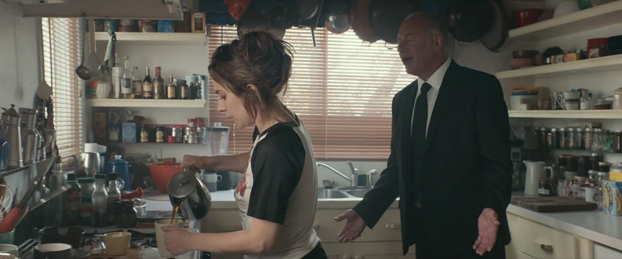 A Star Is Born (2018) movie still: medium — A cluttered residential kitchen with open shelves filled with cookware and jars. A young woman pours…