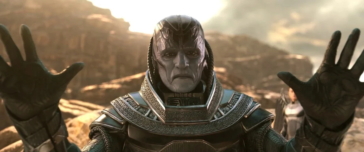 X-men (2000) movie still: medium — A figure with gray skin and metallic armor stands in a rocky desert landscape. The subject faces forward with…