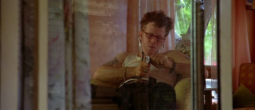 Short Cuts (1993) movie still: medium — A man sits in a domestic space with pink window curtains behind him. The man is holding a stethoscope…