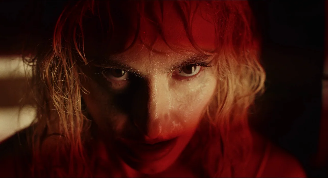Wake Up Dead Man (2025) movie still: closeup — A close-up shot focuses on a woman's face within a dark environment. The woman stares intently at the…