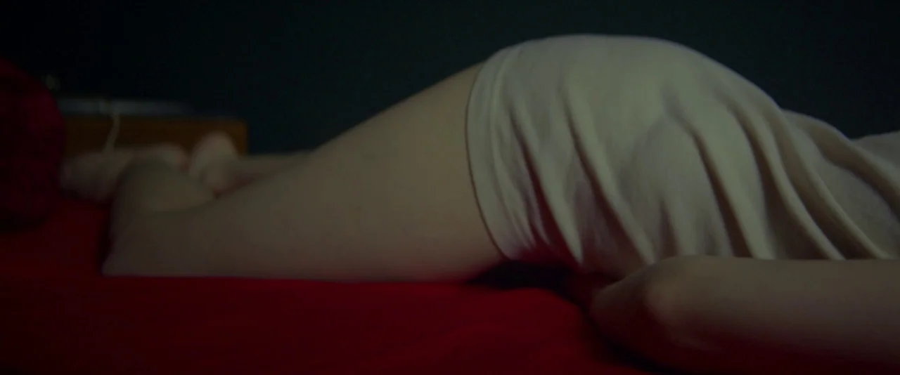 Kissing Candice (2017) movie still: closeup — A close-up view of a person lying on their side on bright red linens. The lower body and legs are…