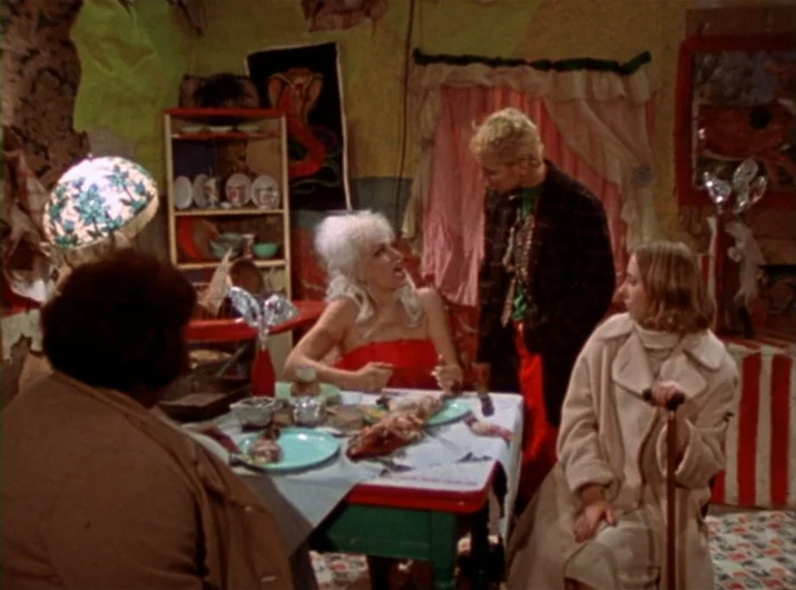 Desperate Living (1977) movie still: medium — A cluttered room features mismatched decorations, including a cobra wall hanging and floral curtains.…