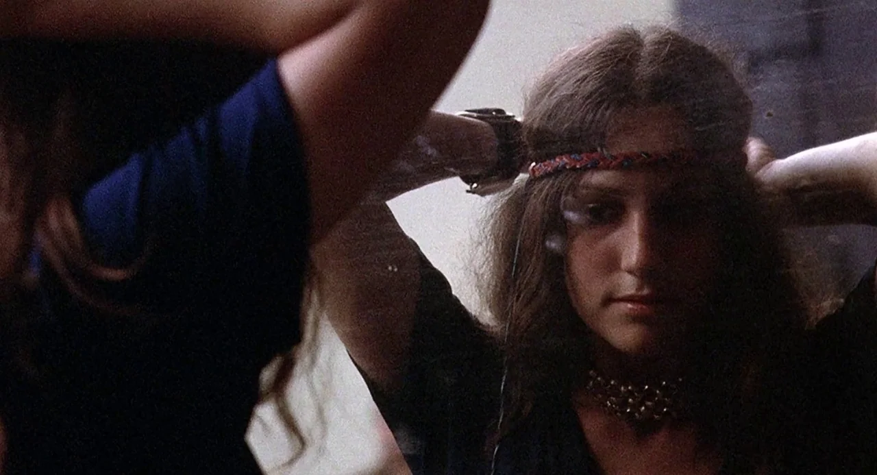 Taking Off (1971) movie still: closeup — A woman looks into a mirror in a dimly lit interior room. She is adjusting her hair and wearing a braided…