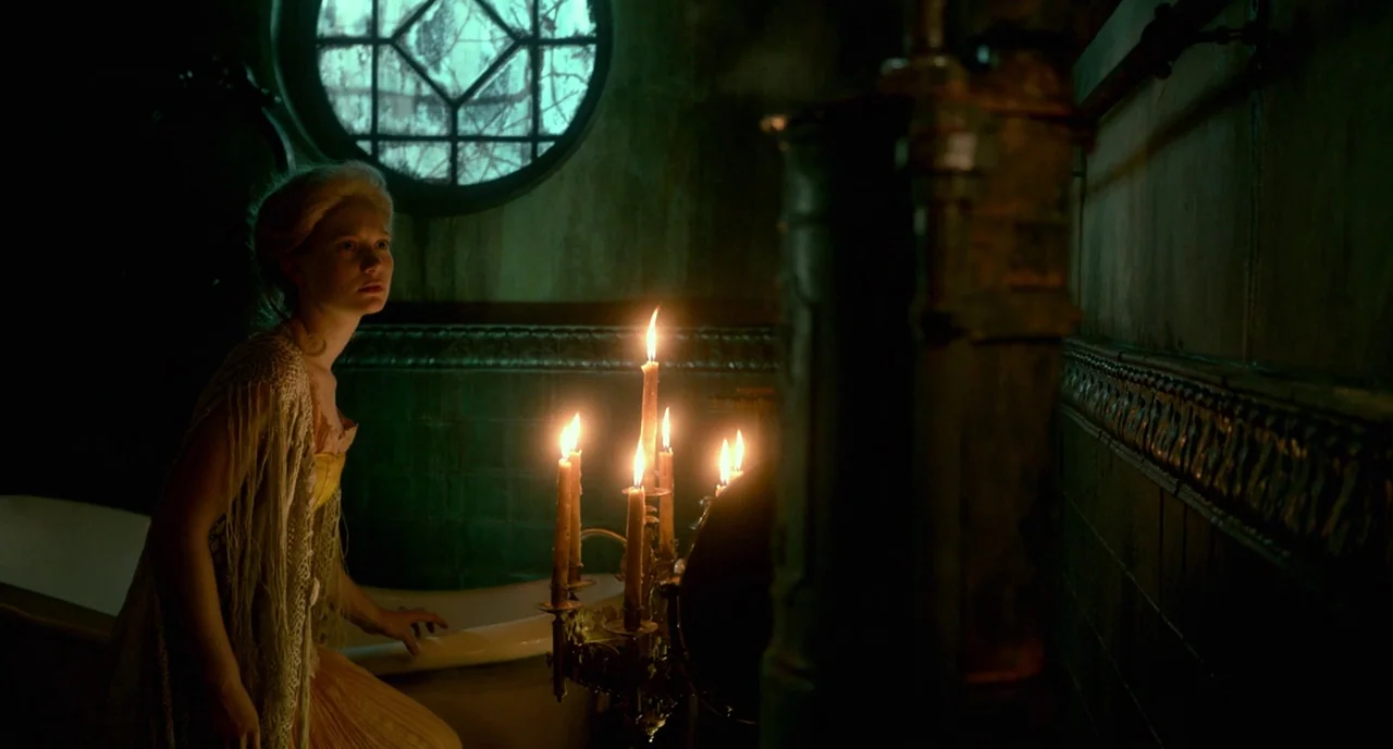 Crimson Peak (2015) movie still: medium — A dimly lit room features teal tile walls and a circular window. A young woman in a gown reaches toward a…