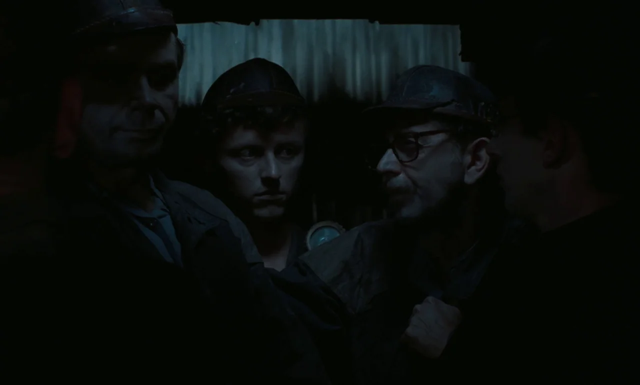 Larks On A String (1969) movie still: medium — A cramped, dark underground passage features corrugated metal walls and dimly lit surroundings.…