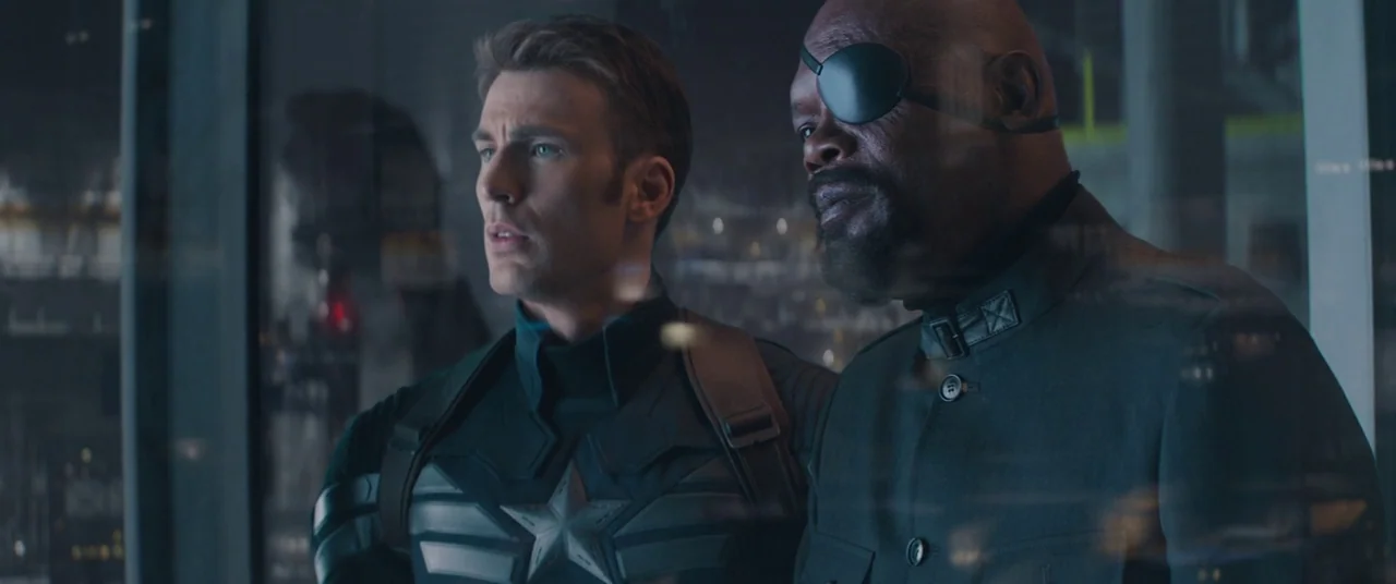 Captain America: The Winter Soldier (2014) movie still: medium — Two men stand before a large glass window in a dimly lit, high-tech interior. They…