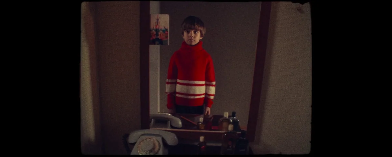 Petrov’s Flu (2021) movie still: medium — A young boy stands in front of a rectangular mirror reflecting his image. Various bottles and a rotary…
